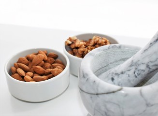 Two white containers with almonds, walnuts  near a marble mortar.