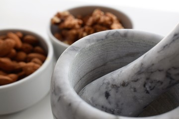Three white containers with almonds, walnuts and a mixture of sunflower, sesame and chia seeds near a marble mortar.