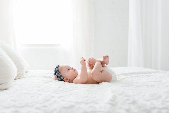 A Six Month Old Baby Grabbing Her Toes On A Neutral Bed