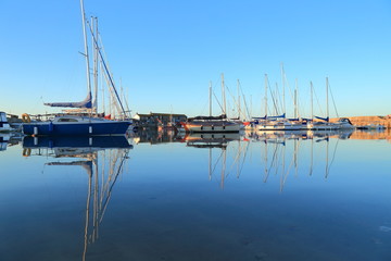 Sailing boats reflected on the water in Lyme Regis harbor called the Cobb