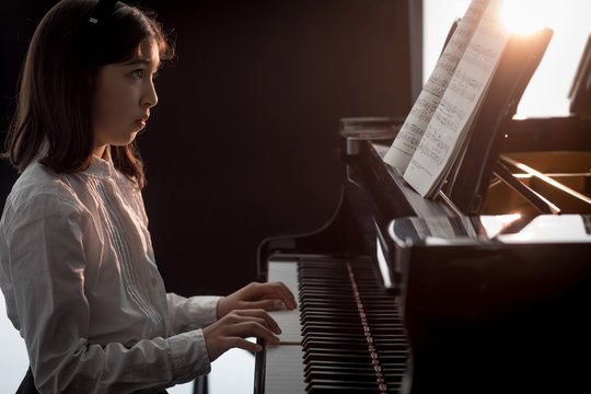 Side view of girl looking at musical note while playing piano
