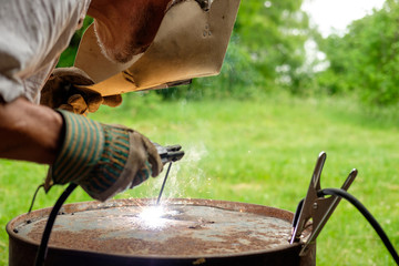 Welder repairs metal barrel, using electric weld