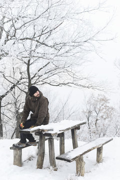 Young man sitting on the table at the park that is covered in snow in the wintertime