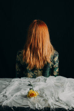 ginger woman backward with a yellow rose on the plastic tablecloth