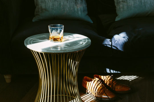 The end of the week. A glass of whisky, a neck tie and brown brogue shoes in a modern room setting. Dramatic lighting.