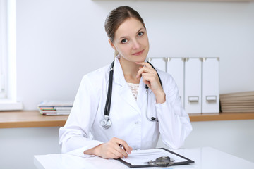 Doctor woman filling up medical form while  sitting at the desk. Medicine and health care concept