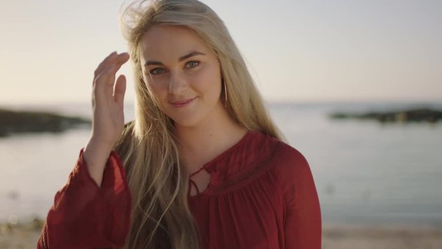 close up portrait of beautiful young blonde woman on beach smiling flirty runs hand through hair feeling confident
