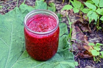 red raspberry jam in an open glass jar on a green leaf on the street