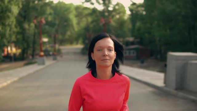 slow motion portrait young woman running outdoors. caucasian girl with black hair wearing red sportswear