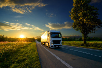 Truck driving on the asphalt road in rural landscape at the golden sunset