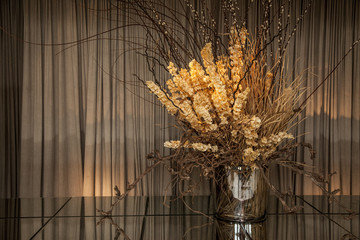 Glass vase with dried flowers on top of a mirror table.