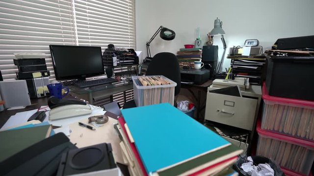 Dolly across cluttered desk in messy office with piles of files.