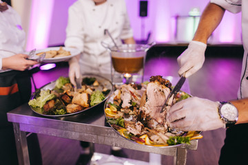 Chef in hotel or restaurant kitchen cooking, only hands, he is cutting meat or steak for a dish on plate.