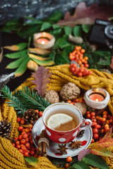 Flat lay view of autumn leaves,candles  and textured scarf on wooden background with cup of tea . Autumn or Winter concept.