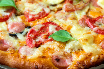 Tasty pizza with sausage, tomatoes, mozzarella and others ingredients on a wooden background.