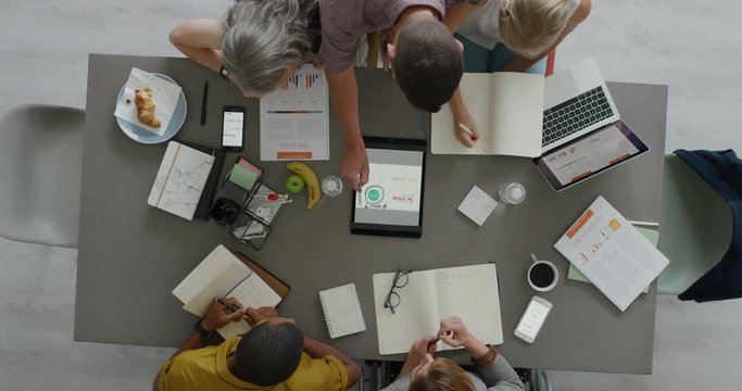 multi ethnic business people graphic designers working startup company project brainstorming ideas using tablet viewing logo designs in office boardroom meeting top view