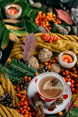  Flat lay view of autumn leaves,candles  and textured scarf on wooden background with cup of tea . Autumn or Winter concept.
