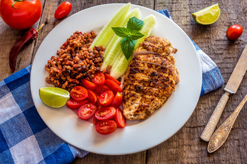 Healthy food. Plate with fried chicken, wheat grains, tomatoes, cucumber and lime on wooden background.