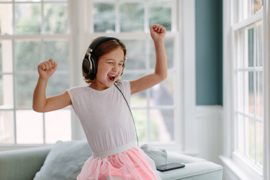 Naklejki Cute young girl listening to music wearing headphones