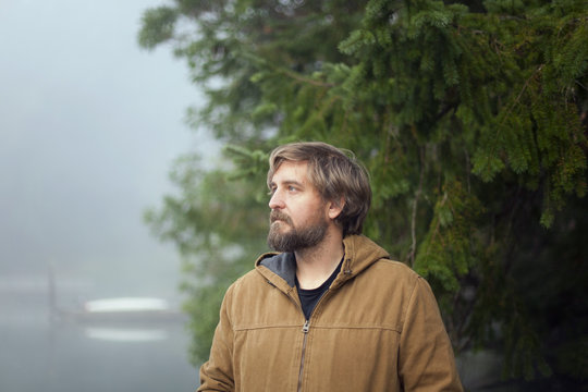 Man in hooded jacket stands on a dock in Fletcher Bay on a foggy morning.