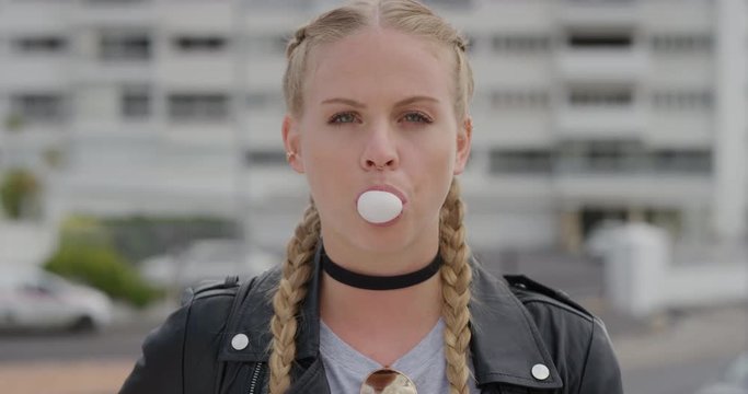 portrait attractive young blonde woman blowing bubblegum looking relaxed enjoying sunny urban day wearing stylish leather jacket independent female in city slow motion