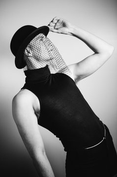 Elegant man wearing bowler hat with veil and rollneck top, cabaret style studio shoot.
