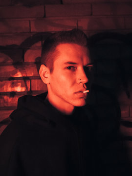 Young man with filter in his mouth looking at camera. Red light. High ISO image.