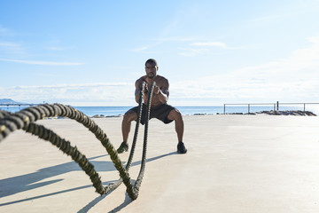 Topless muscular man with ropes at sea.