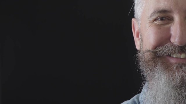 half face portrait of mature bearded man looking at camera smiling cheerful enjoying success satisfaction caucasian male on black background copy space close up