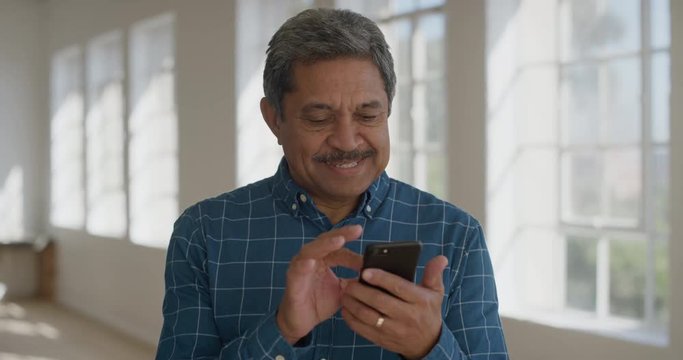 portrait of mature mixed race man using smartphone mobile technology texting browsing social media app enjoying online banking connection