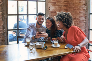 Portrait of happy friends browsing the Internet via cell phone while having cup of coffees in cafe during lunchtime.