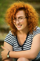 Fototapeta premium Young woman with ginger hair sitting on a steps in a park