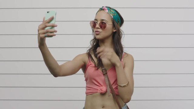 portrait of beautiful stylish young hispanic woman posing taking selfie photo using smartphone camera technology wearing sunglasses sharing online texting social media