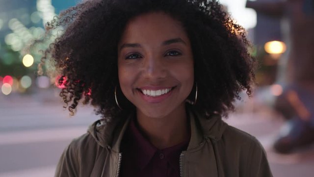 portrait of stylish young black woman with afro smiling happy at camera enjoying night life in urban city
