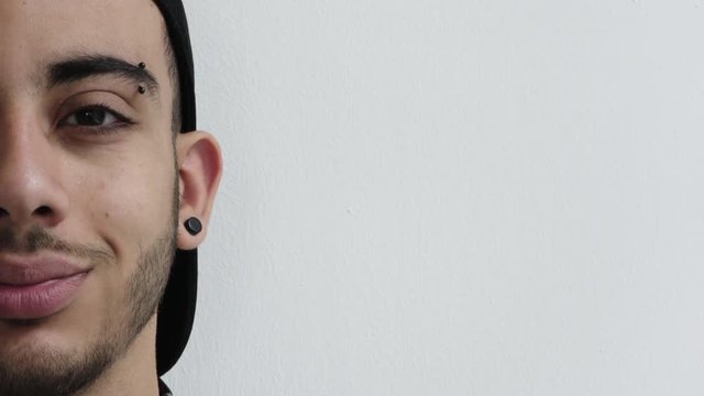 close up half face young hispanic man smiling happy wearing piercings on white background copy space