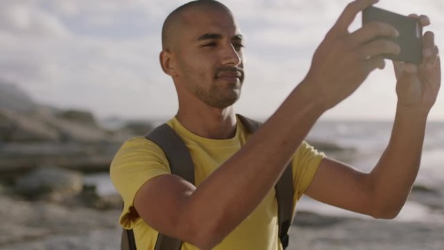 young attractive hispanic man taking photo at beach using phone smiling happy