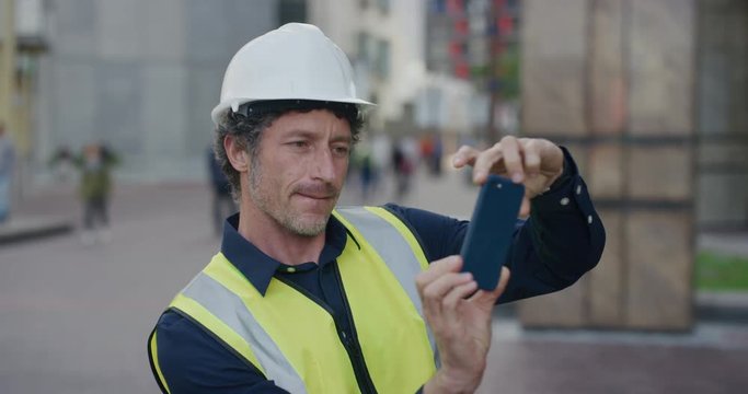 portrait mature construction worker man using smartphone taking photos engineer working on site wearing safety helmet reflective clothing in city slow motion