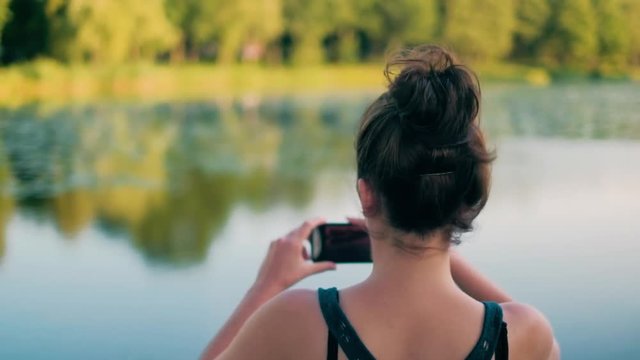 Mid handheld shot of young sporty girl taking photos by smart phone, capturing beautiful lake, travel mobile photography concept, shot in 4K UHD