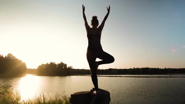 Silhouette of young sporty woman practicing yoga by the lake, late summer evening, relax meditation concentration concept, shot in 4K UHD