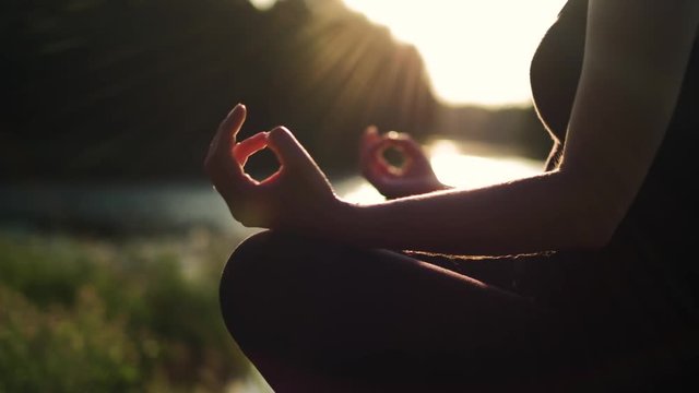 Young healthy girl practicing yoga by the lake at summer evening, shallow dof, close up on girls hand, fitness health nature energy concept, shot in 4K UHD