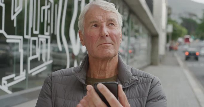portrait of elderly caucasian man using smartphone texting browsing online sending sms message on mobile phone technology app on urban city street