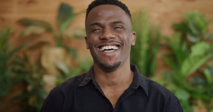 portrait of attractive young african american man laughing excited enjoying successful lifestyle wearing black shirt slow motion