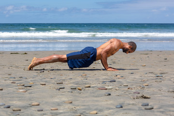 Athletic man at the beach doing yoga on the sand in High Plank pose