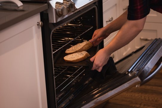 Woman Putting Slice Of Bread Inside The Owen In Kitchen