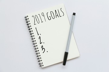 Text 2019 goals on notebook with pen on white background,office desk.