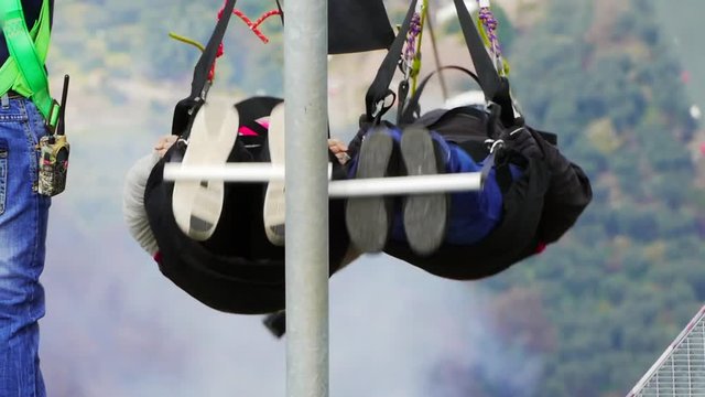 Man assisting tourist to fix carabiner on zip line and prepares them for flight from the mountain. People are securely locked in protective equipment, after staff it breaks the carbine and happy