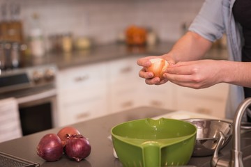 Woman removing peel of onion in kitchen