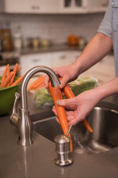 Woman washing carrot in kitchen at home