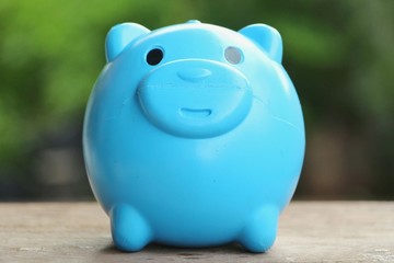 Blue piggy bank on wood table with blur green background.