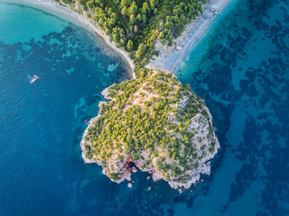 Island reaching out into the big aqua blue ocean at Stafilos beach on the island of Skopelos in Greece. Sunset view from above - obrazy, fototapety, plakaty